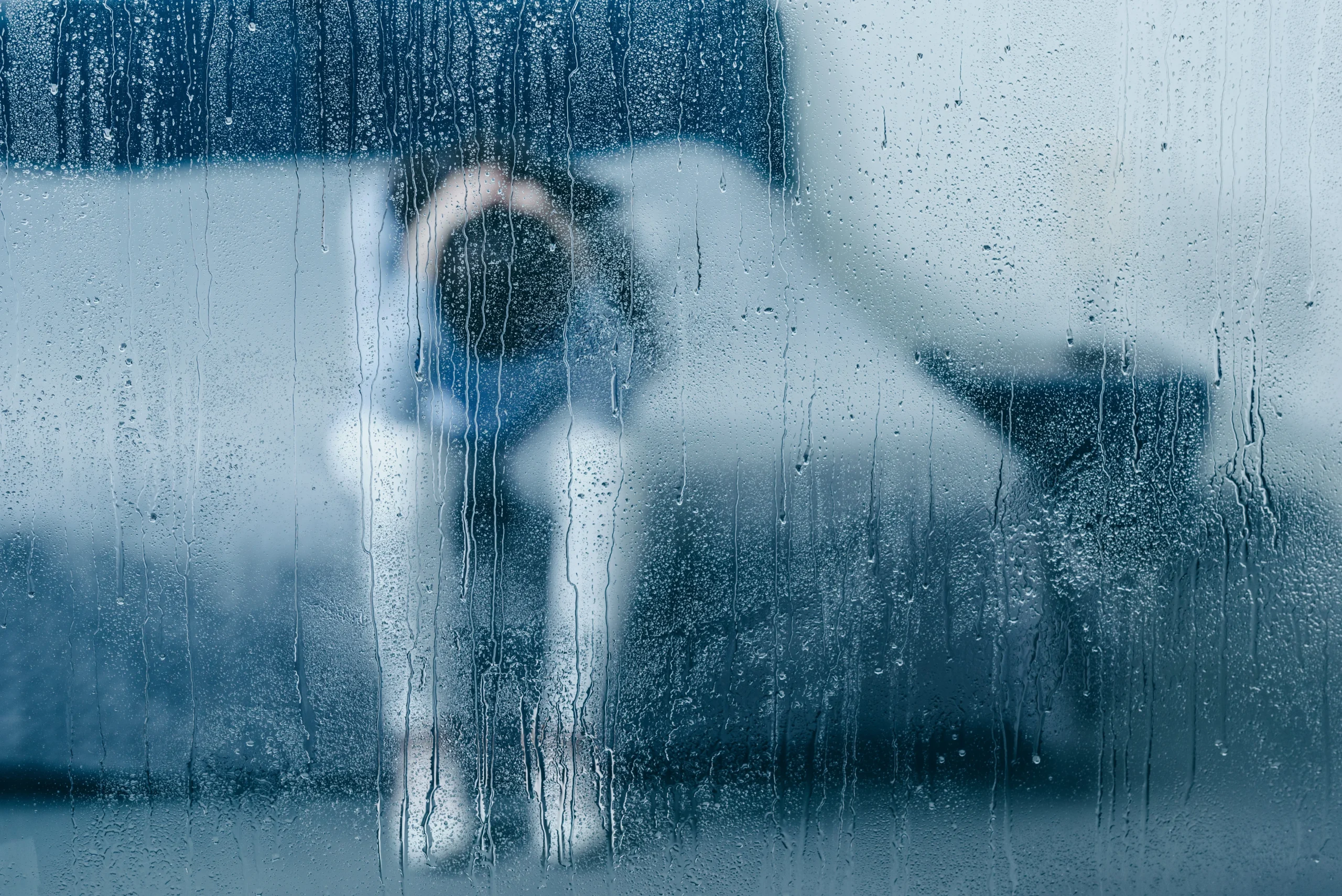 Person standing in the rain looking down seen through a rain-covered window, representing the emotional weight of an antidepressant that has stopped working