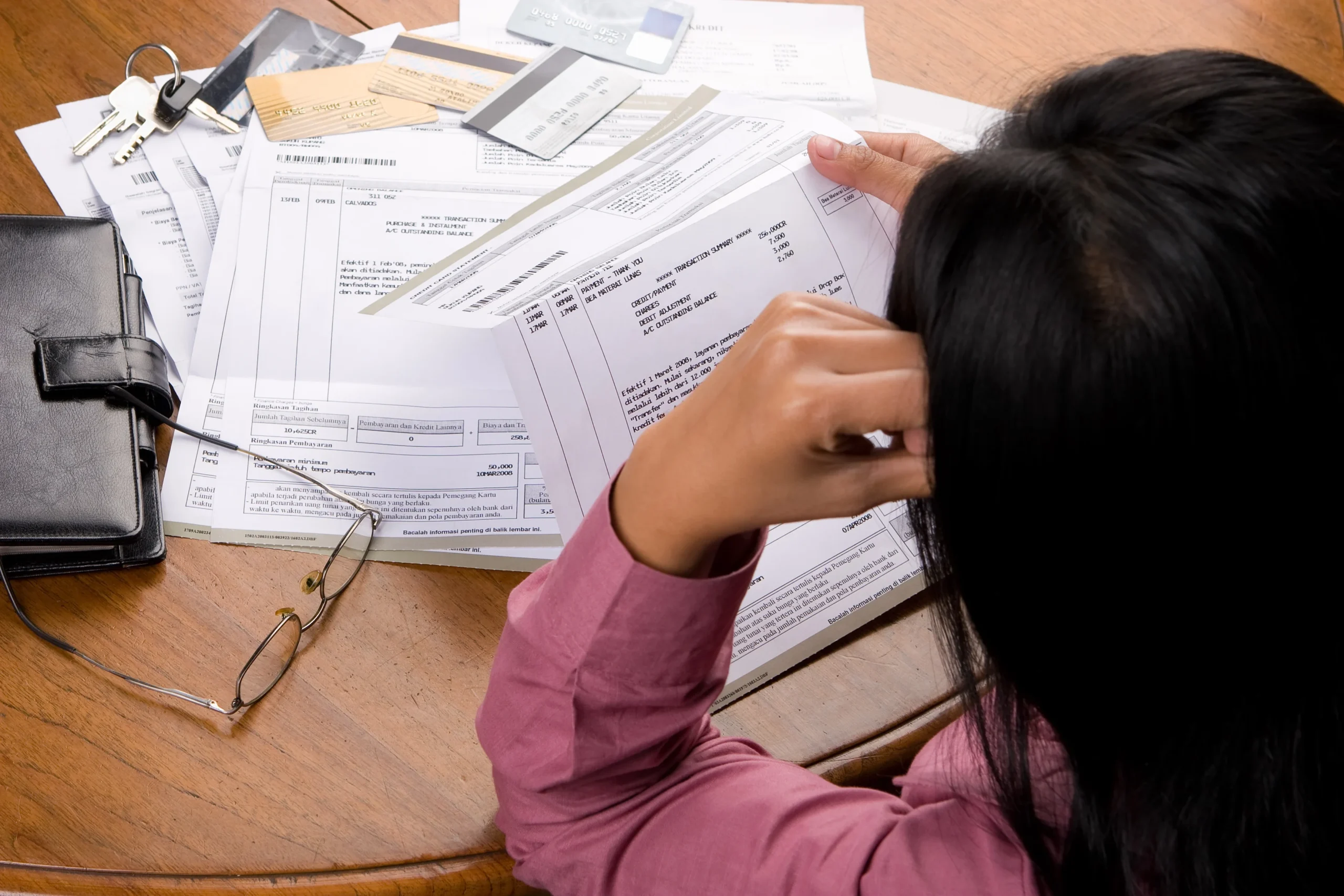 A woman holding her head while reviewing a stack of bills and credit card statements at a table, illustrating the link between financial stress and mental health discussed by Georgia Behavioral Health in Norcross, GA